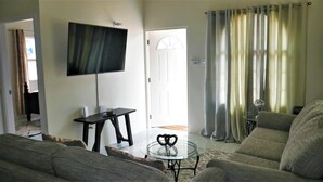 A living room with a flat-screen TV mounted on the wall, a round glass coffee table, and a sofa. - Lux Sea View Camelot Village Discovery Bay (Discovery Bay)