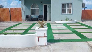 A building with a light blue exterior, a covered entrance, and a paved area with artificial grass and concrete slabs. - Lux Sea View Camelot Village Discovery Bay (Discovery Bay)