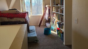 Een kamer met schuine wanden, een bed, een boekenkast en een raam met gordijnen.