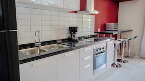 A modern kitchen with white cabinets, a black countertop, a coffee maker, and a microwave. - Adorable 1-bedroom-apartment 2 km From Eagle Beach (Noord)