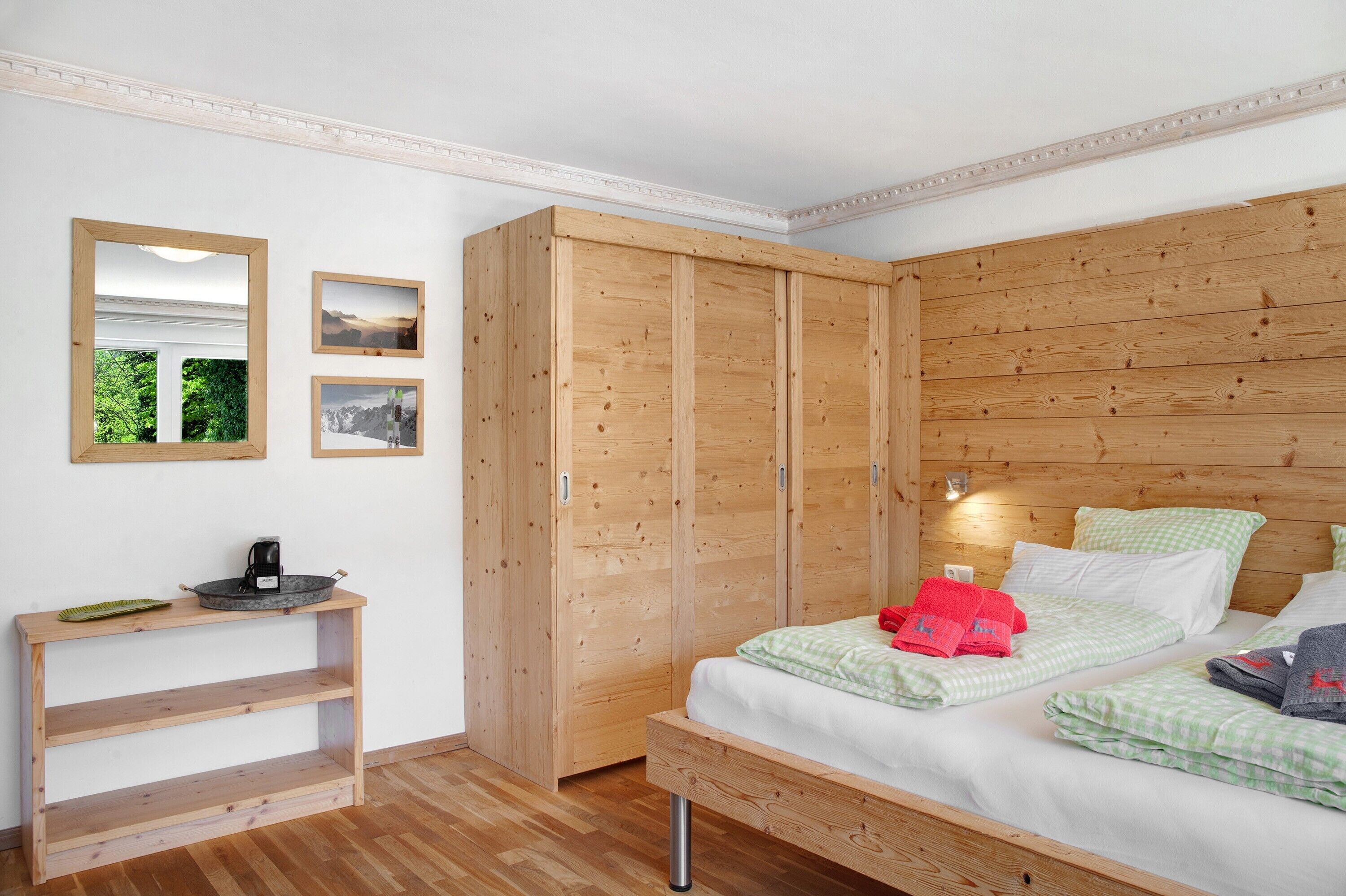 A bedroom with a wooden wardrobe, a bedside table, a bed with green checkered bedding, and two framed pictures on the wall.