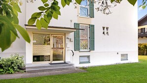 Un edificio moderno con fachada blanca, contraventanas verdes y una pequeña ventana con celosía de metal.
