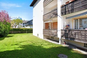 A modern building with a balcony, a well-maintained lawn, and a mountain in the background.