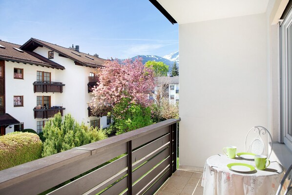 A balcony with a view of a building, a tree with pink blossoms, and a table with a tablecloth and green plates.
