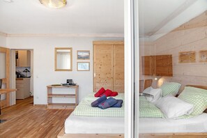 A room with a bed, wooden wardrobe, and a small table with a lamp.