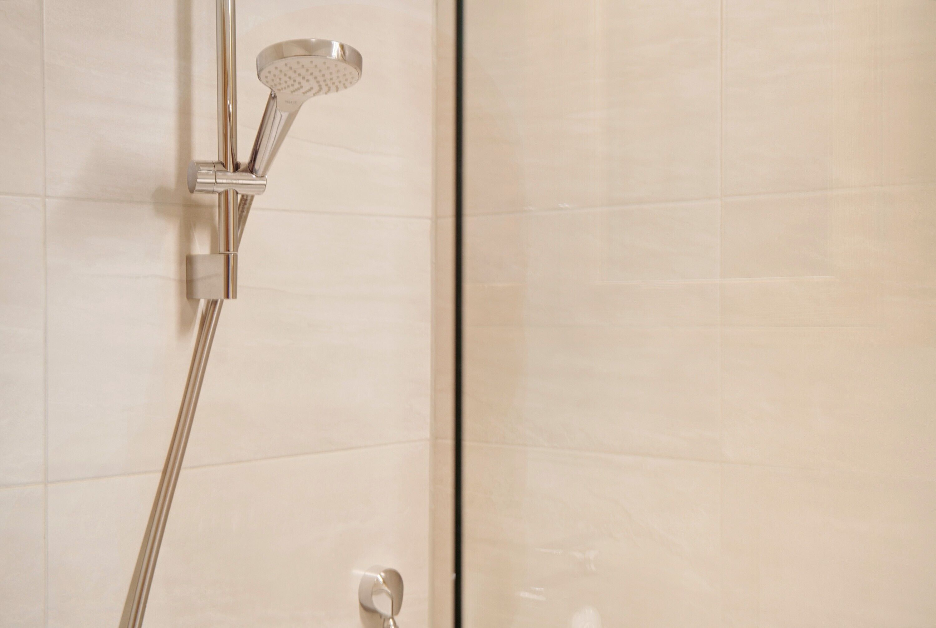 A showerhead with a handheld attachment, mounted on a wall with a tiled surface.