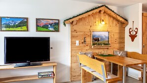 Een houten kamer in chaletstijl met een televisie, een houten bank, een eettafel en twee ingelijste foto's aan de muur.