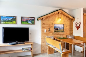 A wooden cabin-style room with a TV, wooden bench, dining table, and two framed pictures on the wall.