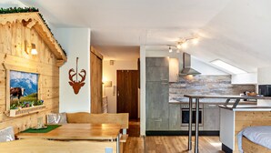 Een modern interieur met een houten eethoek, een keuken met een tegelachtergrond en een slaapkamer op een entresol met een dakraam.