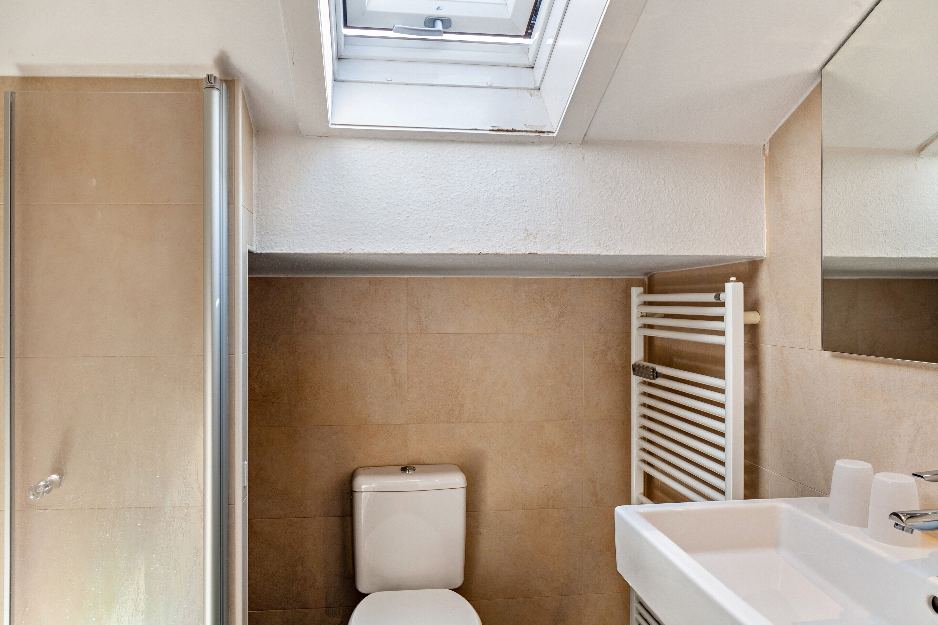 Un baño con tragaluz, inodoro, toallero y lavamanos.