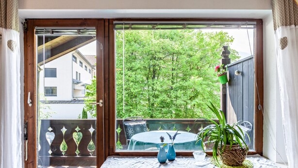 Een kamer met een raam met uitzicht op een balkon, een radiator en een tafel met een vaas en een plant.