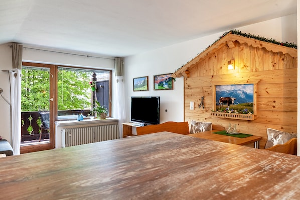 A wooden dining area with a table and chairs, a television, and a window with a view of greenery.