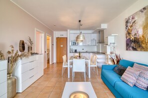 A modern living room with a dining area, white cabinetry, and a blue sofa.