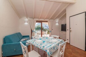 A dining area with a table set for four, a sofa, a TV, and a door.