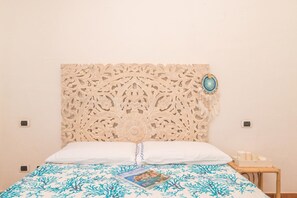 A bed with a patterned bedspread, a decorative headboard, and a small bedside table with a tray of items. - Celeste House With Pool, Pittulongu, Italy (Pittulongu)