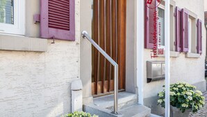 Entrada de un edificio con puerta de madera, barandilla de metal y un letrero con código QR.