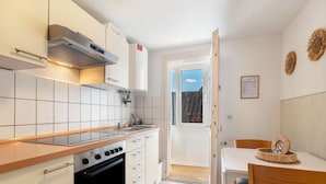 Una cocina con estufa, horno y armarios blancos. Hay una mesa de comedor con sillas y vistas al exterior.