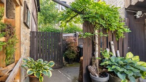 Un estrecho callejón con vallas de madera, plantas en macetas y un pequeño árbol creciendo entre las vallas.