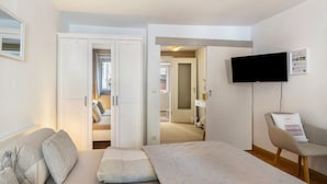 Habitación de hotel con cama, una silla, un televisor montado en la pared y una puerta que da a un baño.