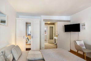 Et hotelværelse med en seng, en stol, et fjernsyn ophængt på væggen og en dør, der fører til et badeværelse.