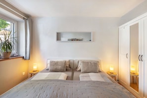 A bedroom with two beds, a bedside table with a lamp, a shelf above the beds, and a wardrobe. - Charming "Enz" Apartment in Bietigheim’s Old Town (Bietigheim-Bissingen)