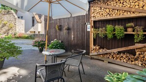 Un patio al aire libre con una mesa redonda y sillas, un paraguas blanco y una cerca de madera con plantas.