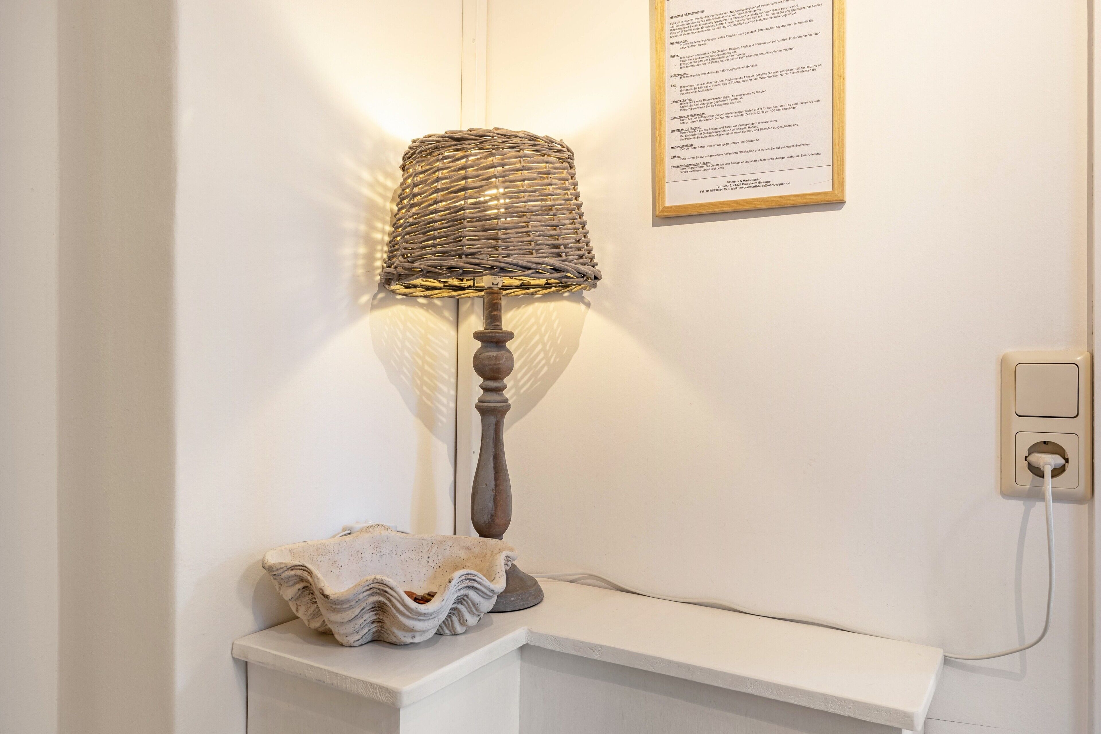A lamp with a woven shade, a textured bowl, and a wall-mounted electrical outlet.