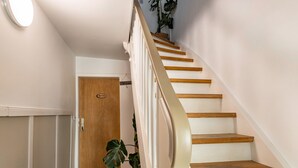 Una escalera con peldaños de madera y paredes blancas que conduce a una puerta de madera con un cartel de 'Welcome'.