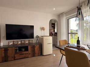A modern living room with a flat-screen TV, a vintage refrigerator, wooden cabinets, and a dining area with a table and chairs. - Landliebe – Studio Apartment Near Lake with Sauna (Petersthal)