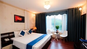 Une chambre d’hôtel avec un grand lit, une table de chevet avec une lampe, une petite table avec une plante et une chaise.