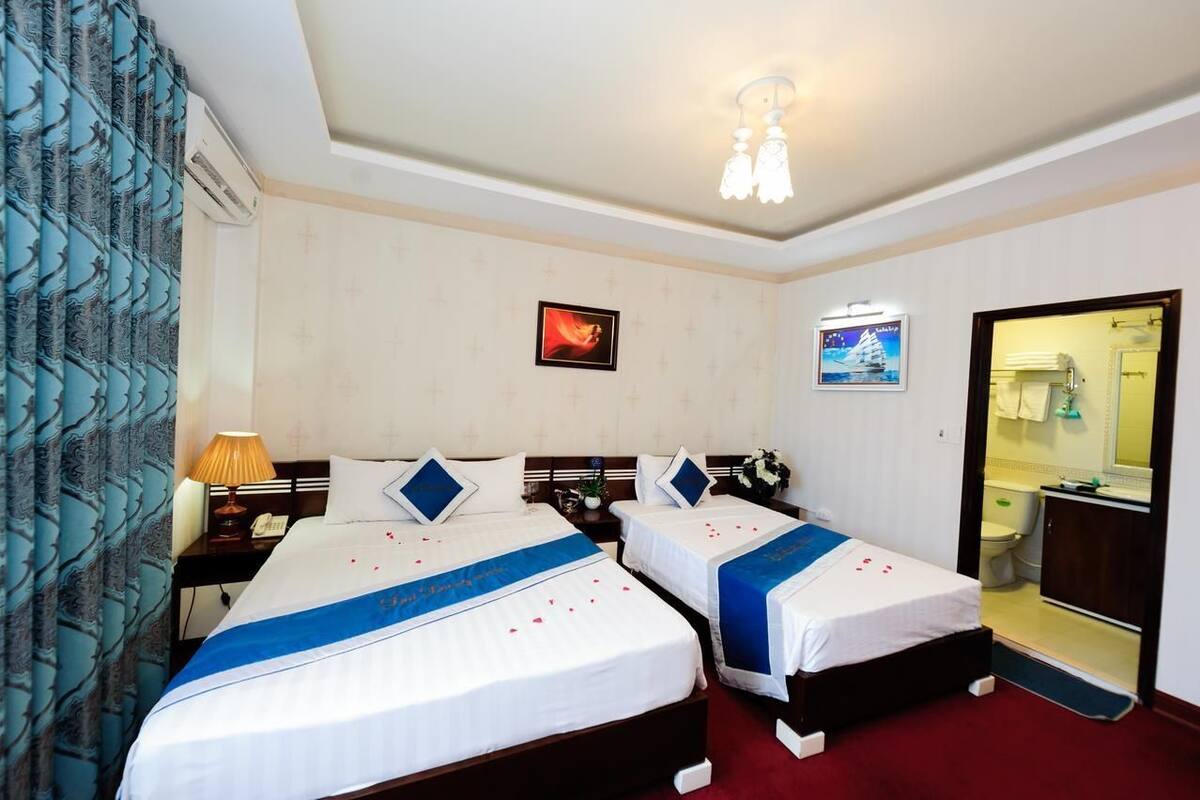 Habitación de hotel con dos camas, una mesita de noche, una lámpara, un espejo y un baño visible a través de una puerta abierta.