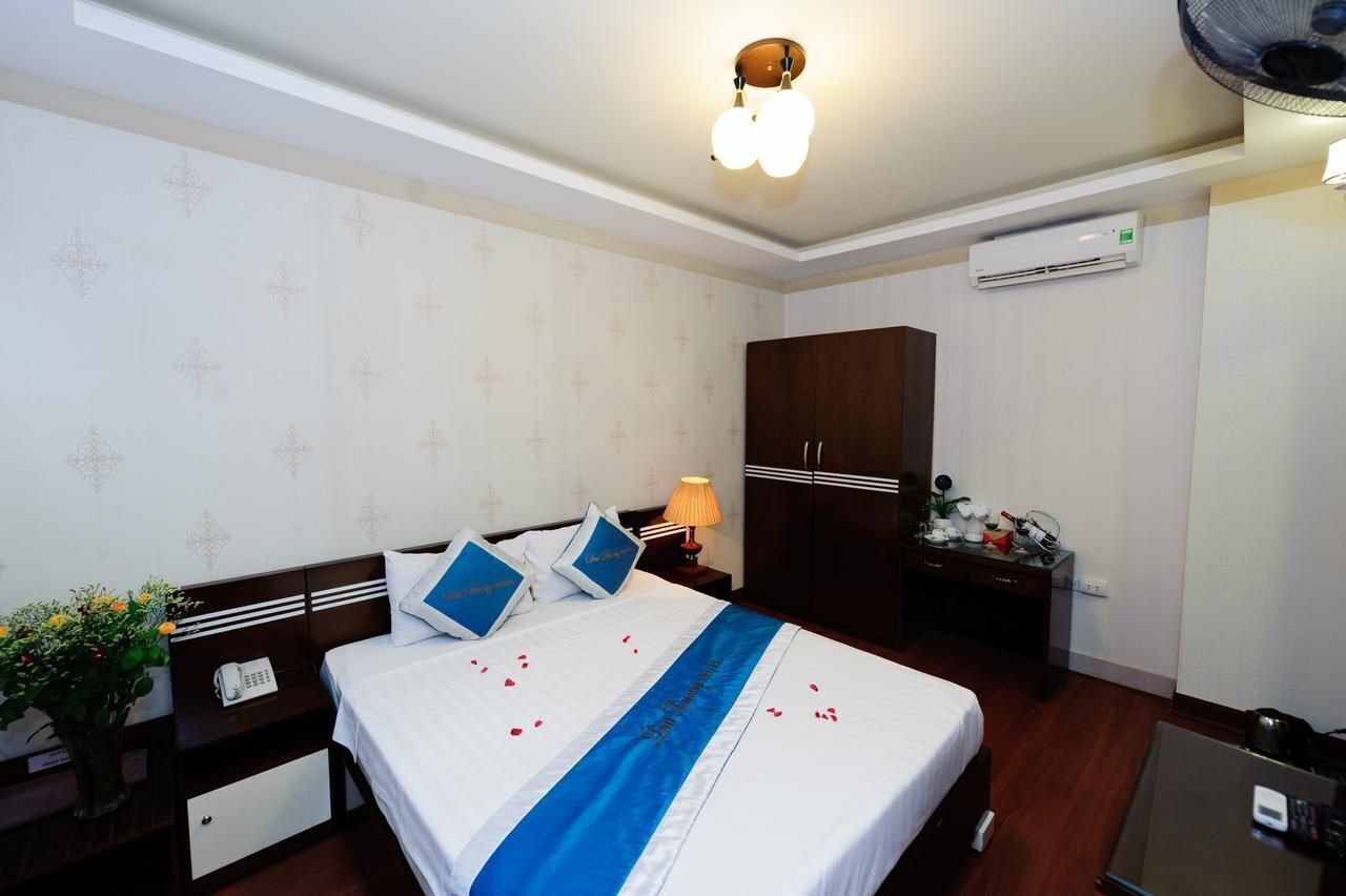 A hotel room with a bed, bedside table, lamp, wardrobe, and an air conditioning unit.