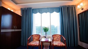 Une chambre d’hôtel avec une grande fenêtre, deux chaises, une petite table et un placard.