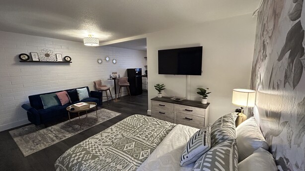 Una sala de estar moderna con sofá, dos sillones, una mesa de centro, televisor, aparador y alfombra estampada.