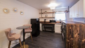 Cocina compacta con paredes de ladrillo blanco, un refrigerador negro, una encimera de madera y un comedor con dos sillas.