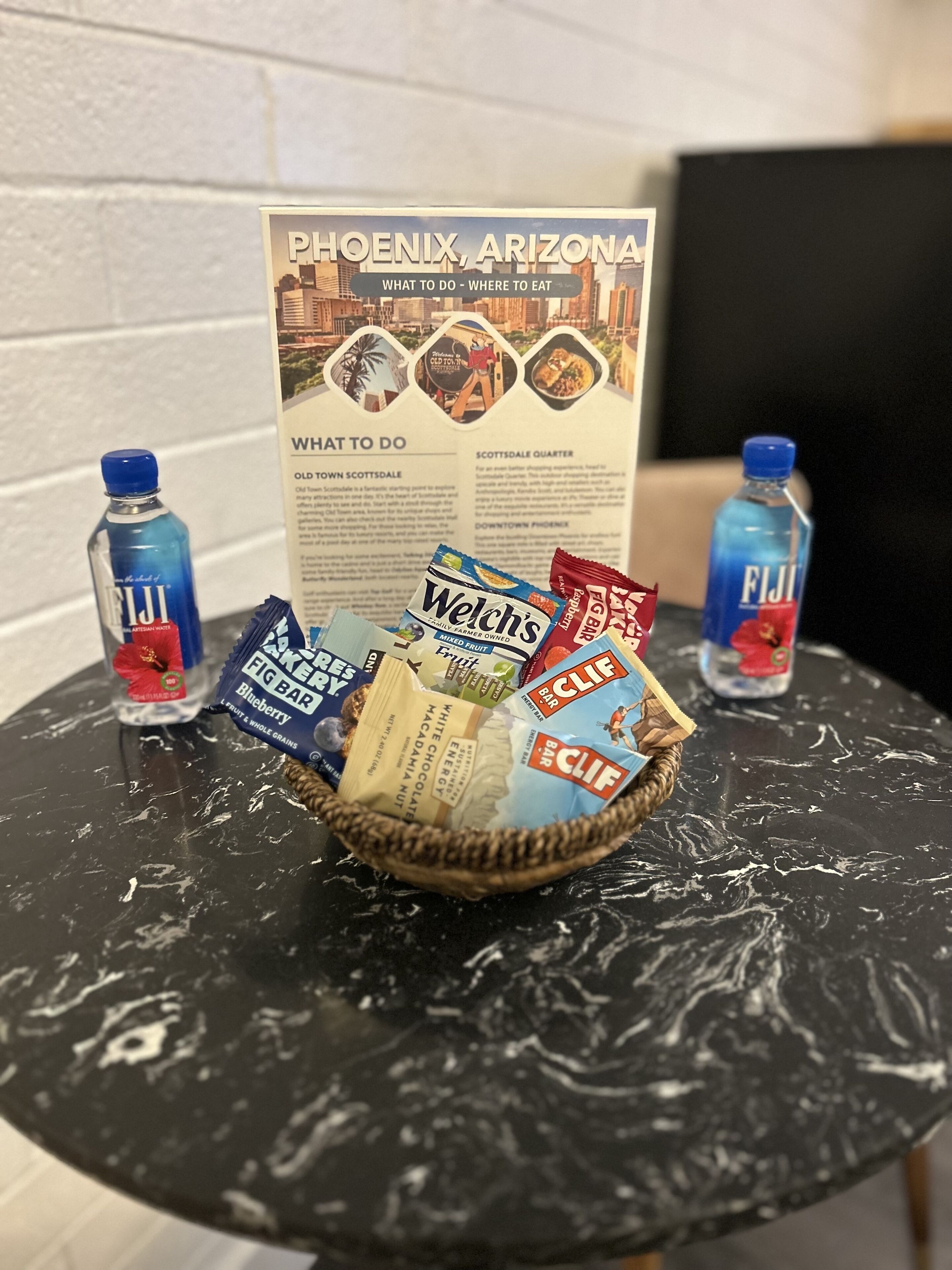 Ein Tisch mit einer Snackkorb, zwei Fiji Wasserflaschen und einer Broschüre für Phoenix, Arizona.