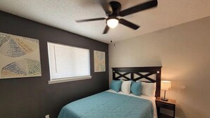 Une chambre à coucher avec un lit, un ventilateur de plafond, une table de chevet et des œuvres d’art murales.