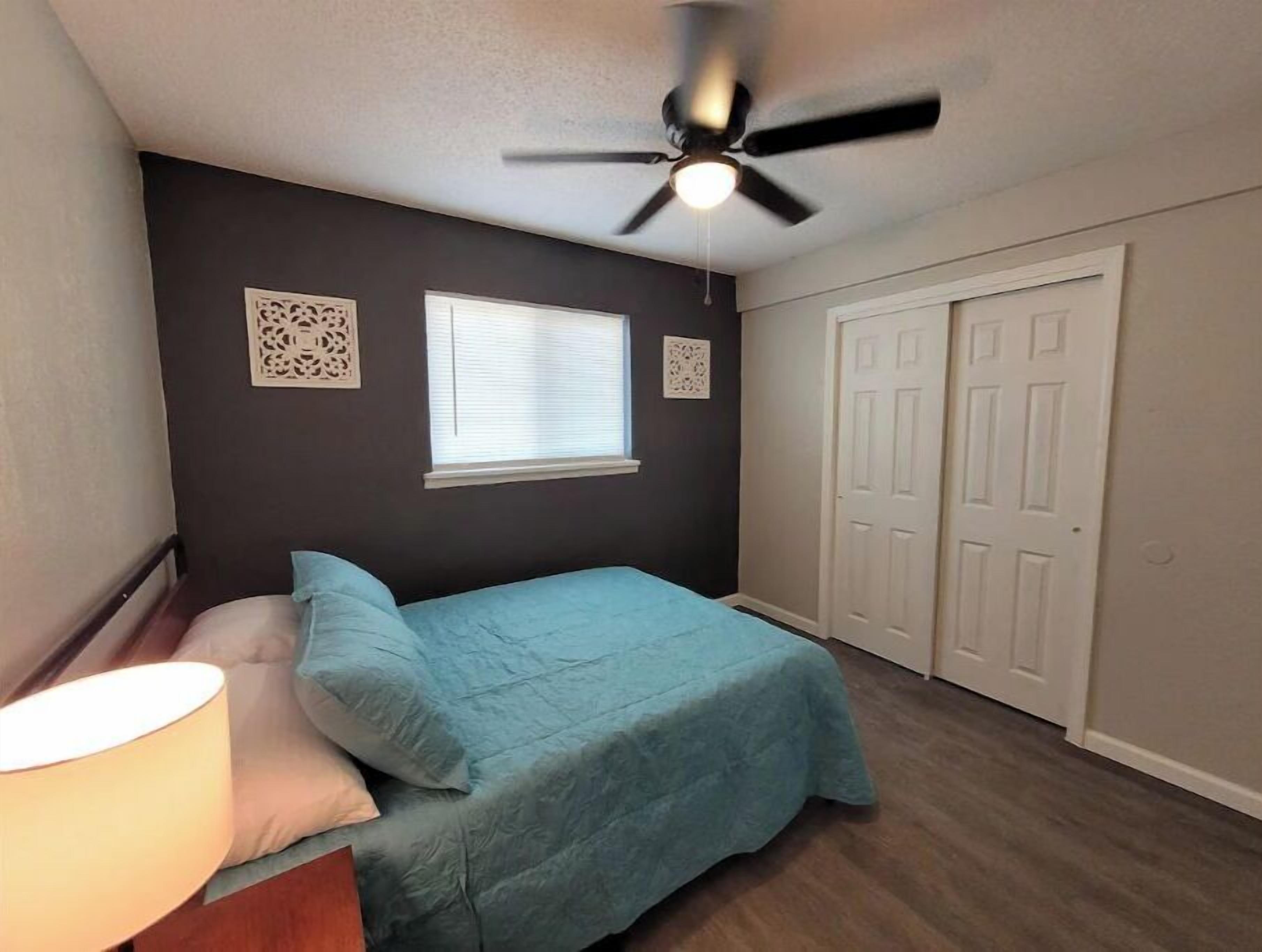 A bedroom with a bed, a ceiling fan, a window, and a door.