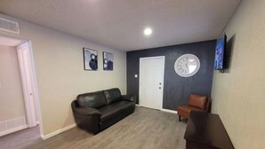 Un salon avec un canapé en cuir marron foncé, un fauteuil en cuir marron, une table basse en bois, une porte blanche et une horloge murale.