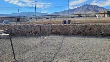 A fenced outdoor area with a stone wall and a metal fence, set against a backdrop of mountains and a clear sky.