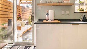Une cuisine moderne avec des armoires blanches, un plan de travail en bois et une porte-fenêtre coulissante donnant sur un espace extérieur aménagé pour se détendre.