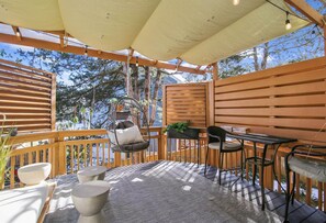 Una terraza techada al aire libre con una silla colgante, una mesa con sillas y vistas a árboles y al cielo.