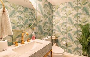 Un baño con lavamanos de mármol, grifería dorada, inodoro y espejo.