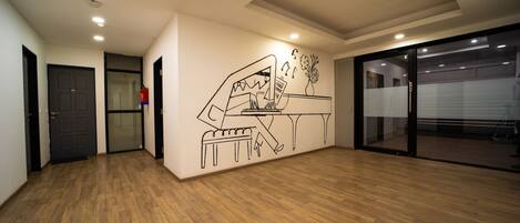 Um quarto espaçoso com piso de madeira, uma ilustração de um piano na parede e uma porta de vidro deslizante que dá para uma varanda.