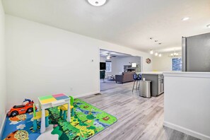 Een moderne keuken met een koelkast, een eethoek met tafel en stoelen, en een speelruimte met een speelgoedauto en een puzzeltafel.