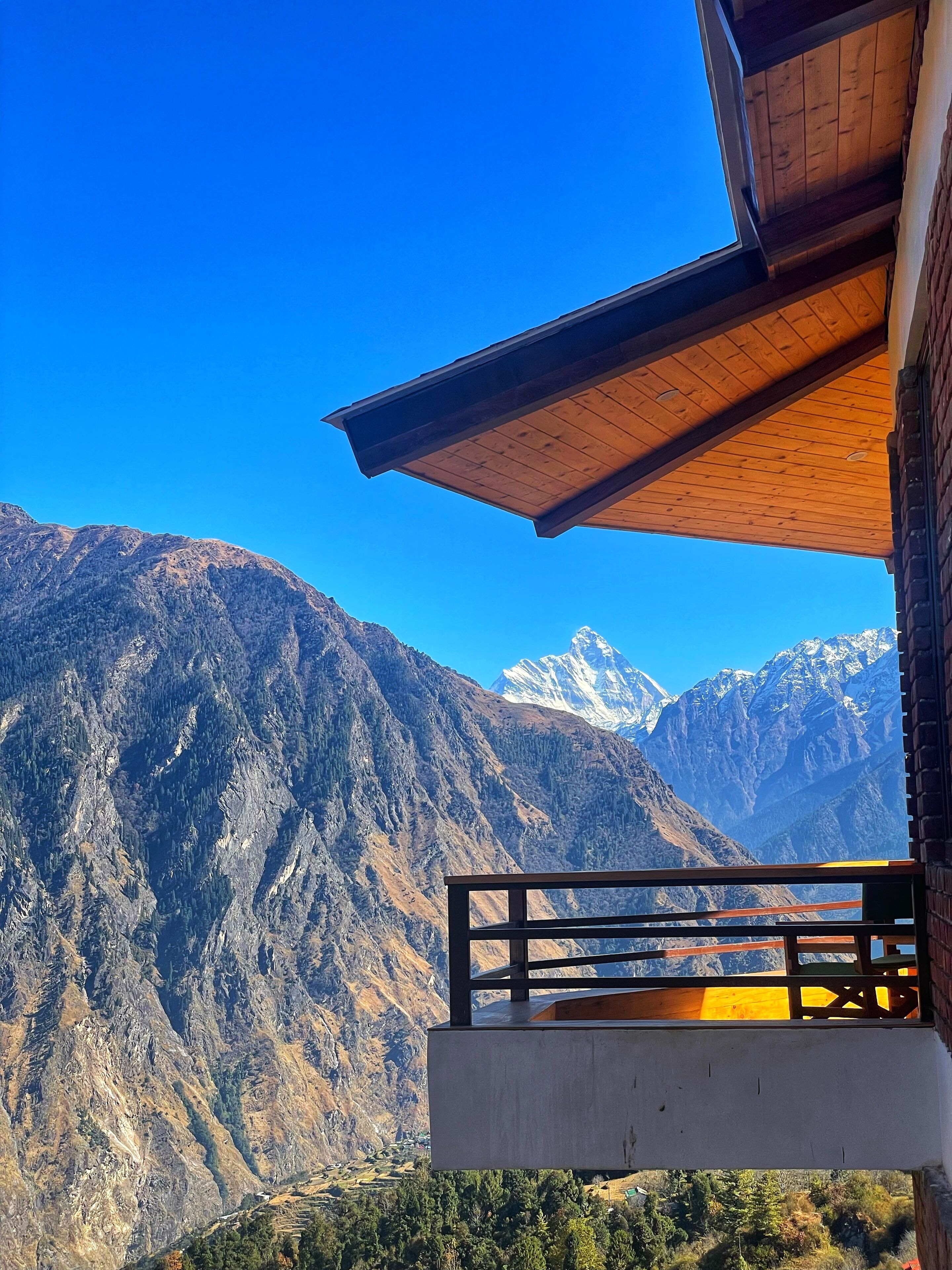 A mountain view from a balcony with a wooden railing and a clear blue sky.