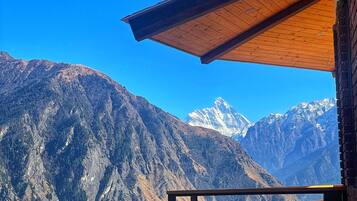A mountain view from a balcony with a wooden railing and a clear blue sky.