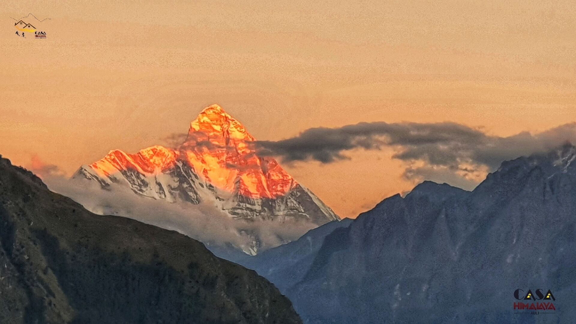 A mountain landscape with a prominent peak, possibly during sunrise or sunset, and a logo in the top left corner.