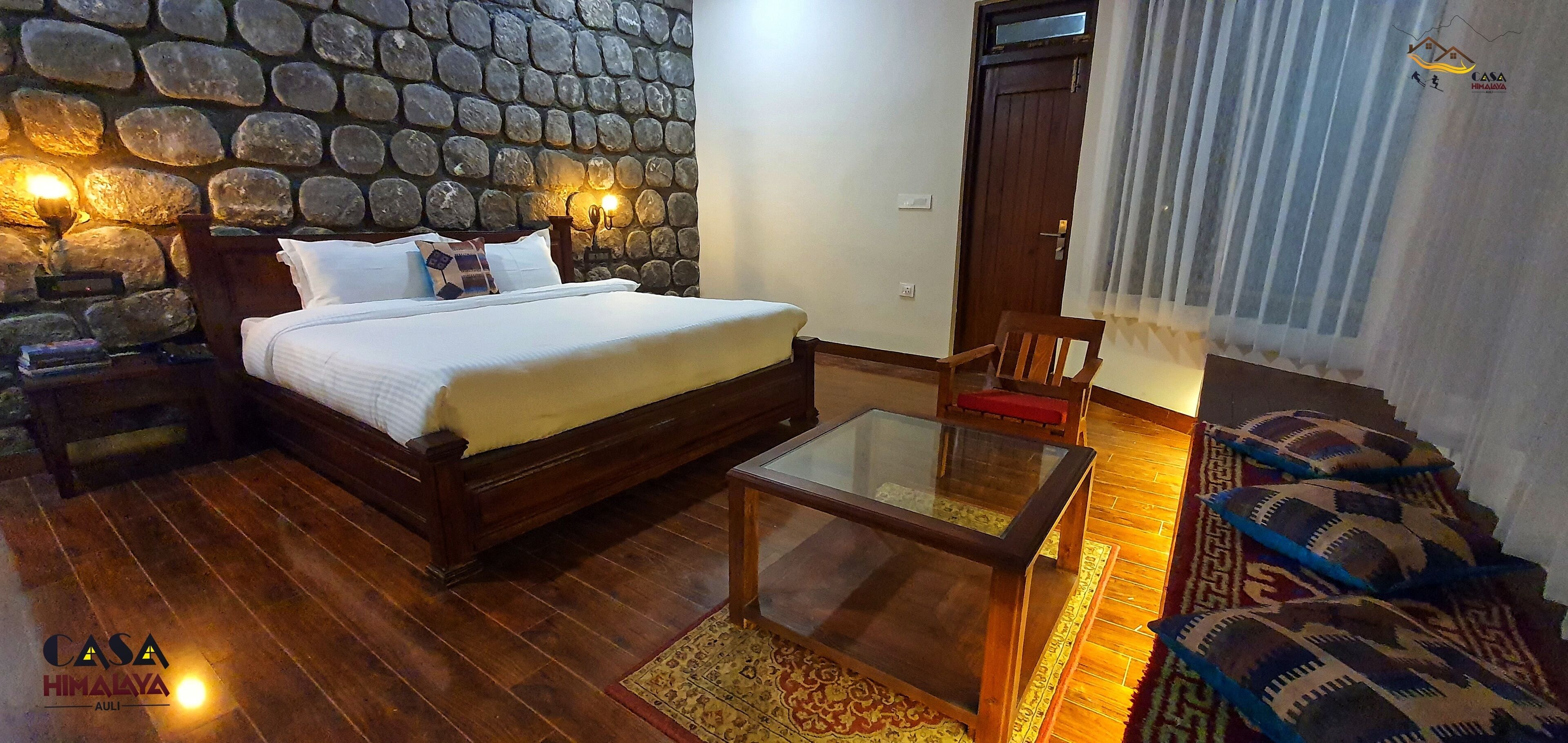 A bedroom with a stone wall, a wooden bed, a glass coffee table, and a patterned rug.
