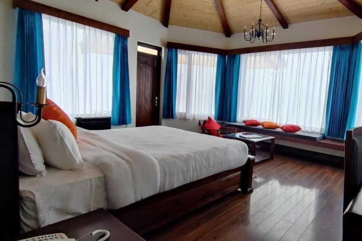 Un dormitorio con una cama grande, un escritorio, una silla y un rincón con ventanilla y cortinas.